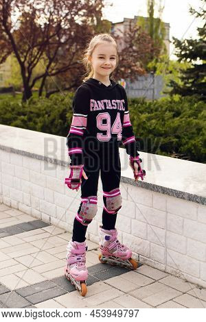 Girl Child Rollerblading In Fall Protection In The Park. A Happy Child Actively Spends His Free Time