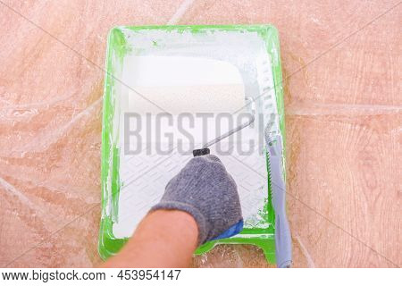 A Man Rolls White Acrylic Paint Into A Paint Tray On A Foam Roller. Painting The Door.