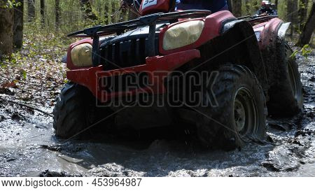 Close-up Of A Red Atv Riding Through A Muddy Puddle In The Spring Forest. Extreme Type Of Outdoor Ac