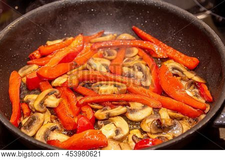 Overhead Shot Of Mushrooms, Red Onions And Red And Yellow Bell Peppers Frying In A Pan With Old Wood