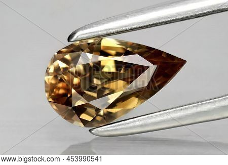 Natural Gemstone Yellow Zircon In Tweezers On A Gray Background