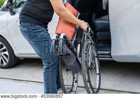 Asian Woman Folding And Lift Up Wheelchair Into Her Car. Accessibility Concept.