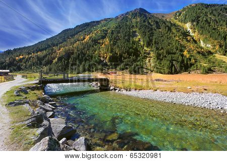 Starting famous Krimml waterfalls. Crystal clear water sparkles in the midday sun. Through the narrow creek wooden bridge spanned. Austrian Alps
