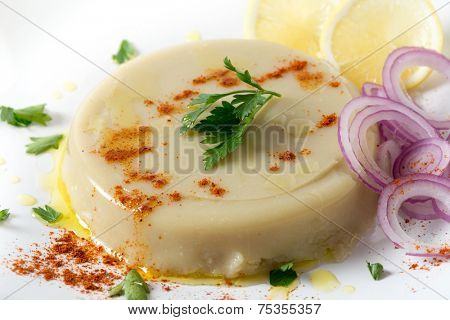 A pate of moulded Turkish dried fava bean puree, garnished with lemon, onion, paprika and parsley, kuru bakla ezmesi