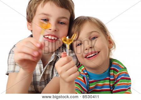 Poco chico y chica sosteniendo piruletas, buscando en él y riéndose, medio cuerpo, aislados en blanco