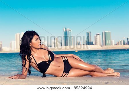 Sexy woman lying on Al Mamzar city beach, Dubai, close to the water