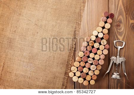 Wine bottle shaped corks and corkscrew over rustic wooden table background and burlap. Top view with copy space