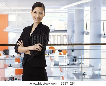 Attractive, happy, asian businesswoman at high-tech business office with arms crossed. Smiling, arms crossed, standing upstairs. Copyspace.