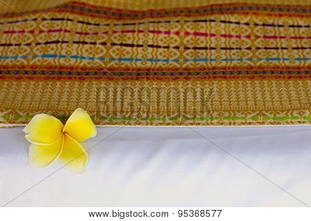 Traditional indonesian woven bed cover over the white sheet, decorated with plumeria flower