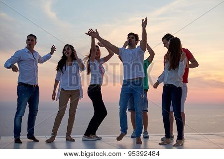group of happy young people dancing and have fun on party in modern home bacony with sunset and ocean in background