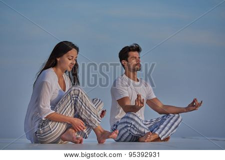 young couple practicing yoga at sunset in modern home terace with ocean and sunset in background