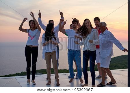 group of happy young people dancing and have fun on party in modern home bacony with sunset and ocean in background