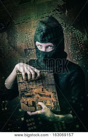 hacker girl in balaclava holding motherboard on a background silhouette drawing circuit board. concept of computer hacking threats.