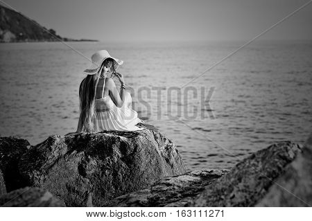 Young girl sits back on the stone on the sea shore