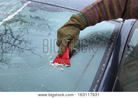 Winter scene human hand in glove scraping ice from windshield of car