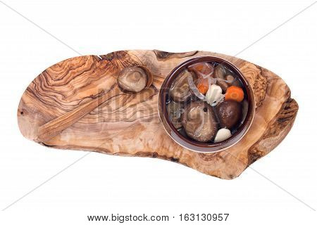 Shiitake marinated mushrooms in ceramic bowl with wooden spoon on olive wood cutting board isolated on white background