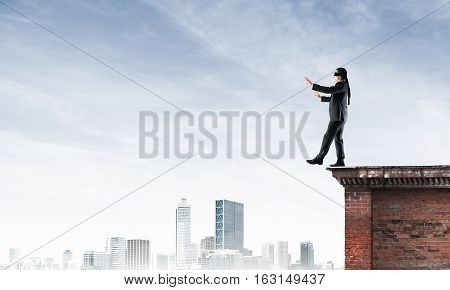 Businessman with blindfolder on eyes walking on building top
