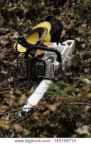 Chainsaw and protective helmet on the forest ground