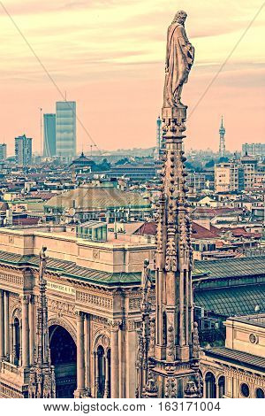 Old photo with view over Milan from the top of the gothic cathedral Milan Cathedral Italy. Church's roof statues in the foreground skyscrapers of the city in the background.Vintage processing.