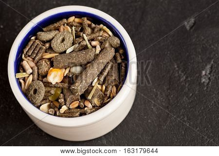 dry food for rodents in bowl on dark background top view.