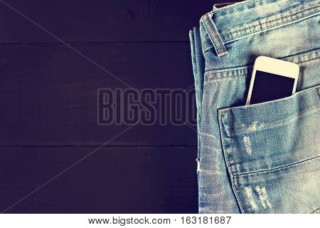 jeans and mobile phone on wooden boards. Phone in your pocket jeans