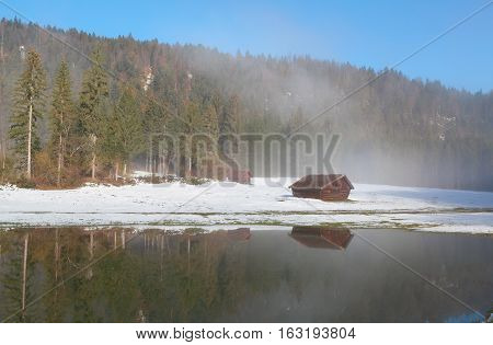 wooden trekker's hut reflected in water in winter foreest