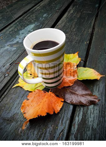 Cup of coffee. Underneath the autumn leaves on wooden table