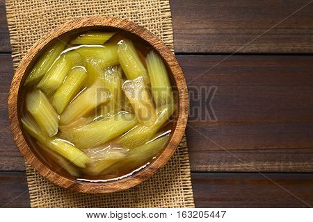 Fresh homemade rhubarb compote in wooden bowl photographed overhead on dark wood with natural light (Selective Focus Focus on the top of the compote)