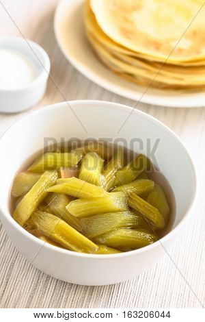 Fresh homemade rhubarb compote in bowl with crepes and powdered sugar in the back photographed with natural light (Selective Focus Focus in the middle of the compote)