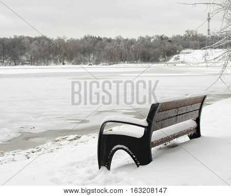snow-covered bench on the bank of a frozen river. Winter landscape