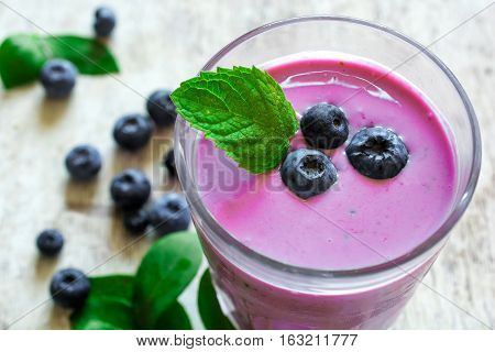 glass of fresh homemade berry smoothie with mint and ripe berries on white wooden background. shallow depth of field. close up
