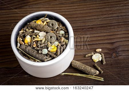 dry food for rodents in bowl on dark wooden background