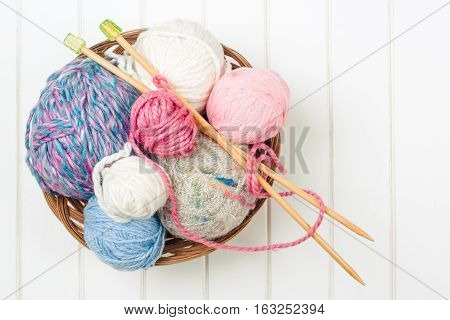 Knitting yarn balls and needles on the white wooden background.