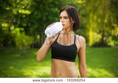 a woman stands on grass and drinking water from a bottle after a workout