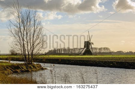 Picturesque backlit image of a polder landscape in the Netherlands on a cloudy day at the beginning of the winter season. In the background a hollow post mill with paddle wheel from 1699.