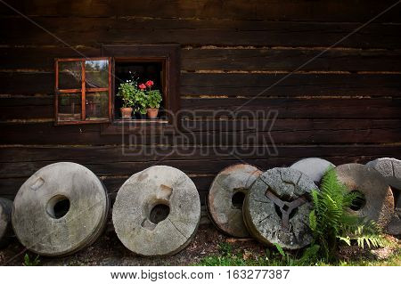 Rustic window with colourful flower pots of geraniums and round grindstones