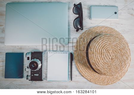 Top view of white surface with laptop, hat, eyeglasses, smartphone, camera on wooden background