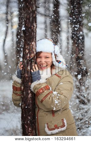 Smiling Woman In Coat With White Fur, Hat With Ear Flaps And Grey Fingerless Knitted Mittens Hugs A