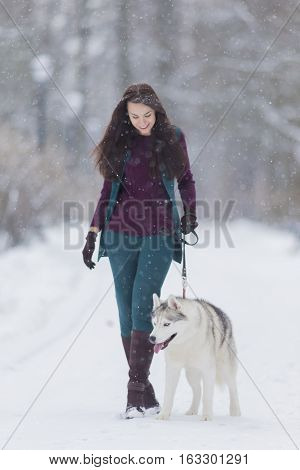 Stylish Caucasian Brunette Woman in Country Style Airing Her Husky Dog in Winter Snowy Forest Outside.Vertical Image