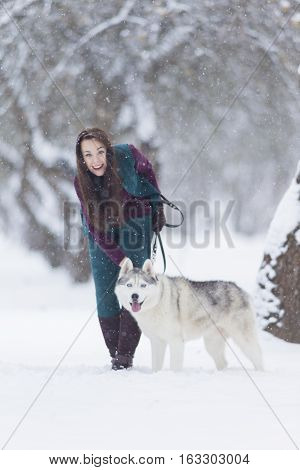 Happy Smiling Caucasian Brunette Woman and Her Husky Dog. Playing Outdoors in Winter White Forest. Vertical Orientation