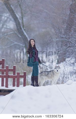 Animals and Pets Concept and Ideas. Pretty Tranquil Caucasian Brunette With Her Husky Dog during a Stroll in Winter.Vertical Shot