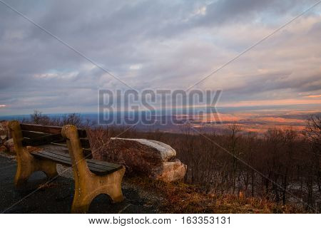 Lone bench faces majestic sunset in purple tones overlooking the valley in winter