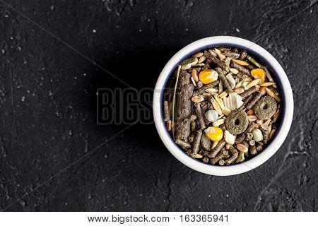 dry food for rodents in bowl on dark background top view.