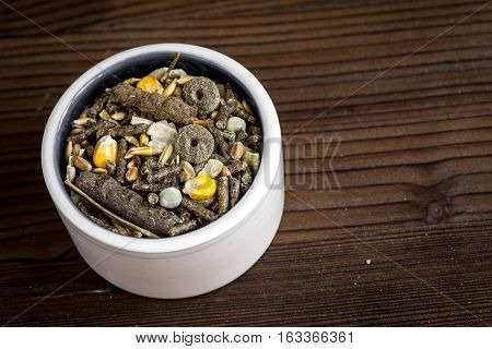 dry food for rodents in bowl on dark wooden background