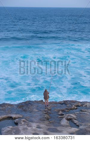 man is fishing in the whale watching season. he stand on the dangerous edge cliff to spend his time with the best leisure