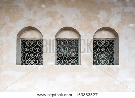 Three old deep windows in row with iron grating. Old vintage building exterior with stone surface.