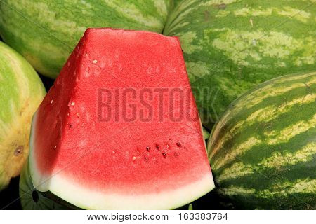 Horizontal image of watermelons stacked together at local market,
one large slice set atop of them, to show how fresh and juicy
they actually are before buying.