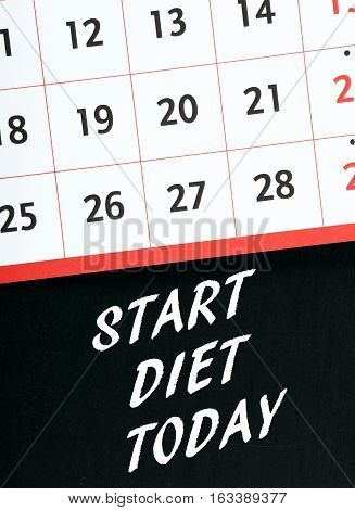 The words Start Diet Today in white text on a blackboard with a wall calendar above as a reminder to change to a healthy lifestyle