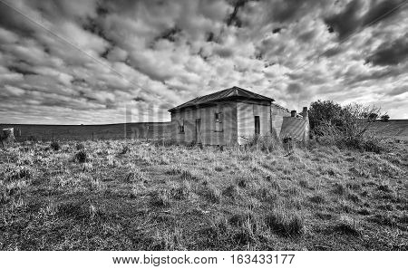 Abandoned farm homstead with corrugated iron roof and walls and boarded up windows left to the elements and now in disrepair
