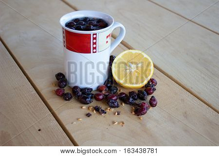 warm rose-hip tea red and white mug dried rosehips whole and crushed half a lemon and everything resting on a wooden table